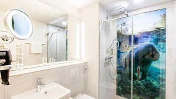 Un baño moderno con un espejo grande, un lavabo, un inodoro y una ducha con mampara que presenta un mural de una criatura marina.