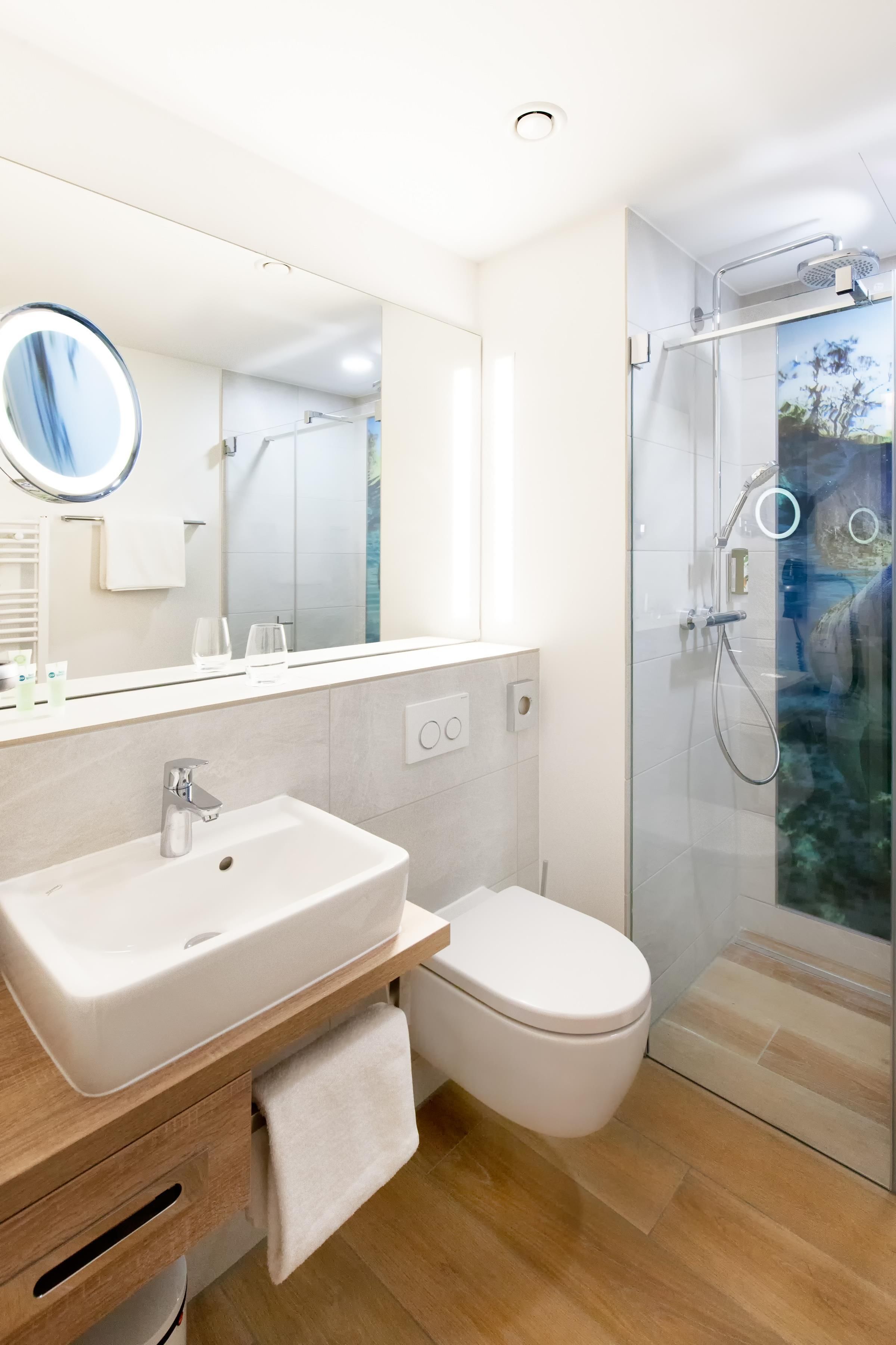 A modern bathroom with a white sink, mirror, and toilet, and a glass-enclosed shower area.