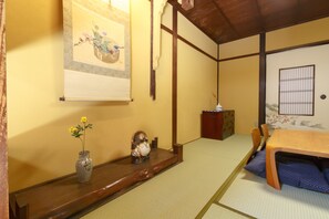 A traditional Japanese room with tatami flooring, a low wooden table, a decorative vase with flowers, and a hanging scroll. - Gojoan (Kyoto)