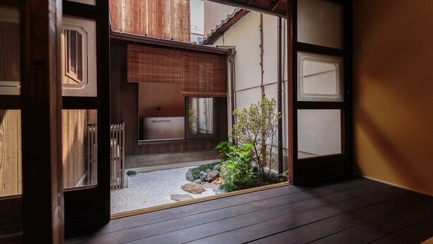 Una habitación japonesa tradicional con suelo de tatami, puertas shoji y un pequeño jardín con rocas y plantas.