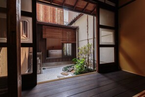 Una tradizionale stanza giapponese con pavimento in tatami, paraventi shoji e un piccolo giardino con rocce e piante.