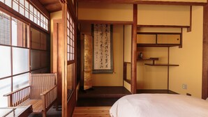 Una habitación japonesa tradicional con suelo de tatami, una cama de madera baja, una puerta corredera y un biombó shoji.