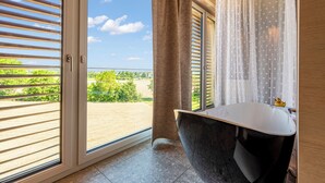 Un baño con bañera, una ventana con persianas y vista a follaje.
