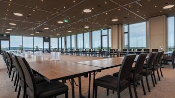 Un salón de conferencias con mesas largas y sillas, ventanas amplias y vistas al exterior.