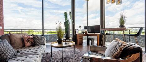 Ein geräumiger Balkon mit einer Couch, einem Sessel und einem Essbereich, mit großem Fenster und einem Blumentopf.