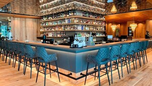Un bar con una barra alargada, estantes llenos de botellas y taburetes azules.