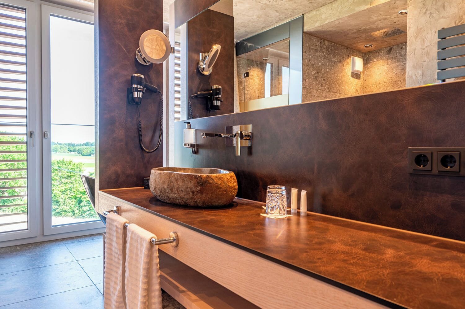 A bathroom with a stone sink, a mirror, a towel rack, and a shower with a glass door.