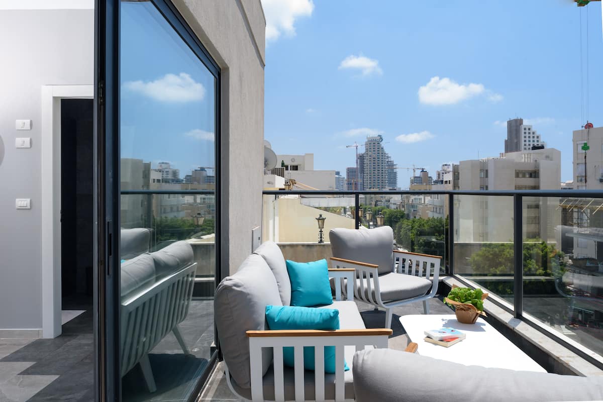 Ein moderner Balkon mit einer Couch, Sesseln und einem Tisch, mit Blick auf eine Stadtlandschaft mit Gebäuden und Bauarbeiten.