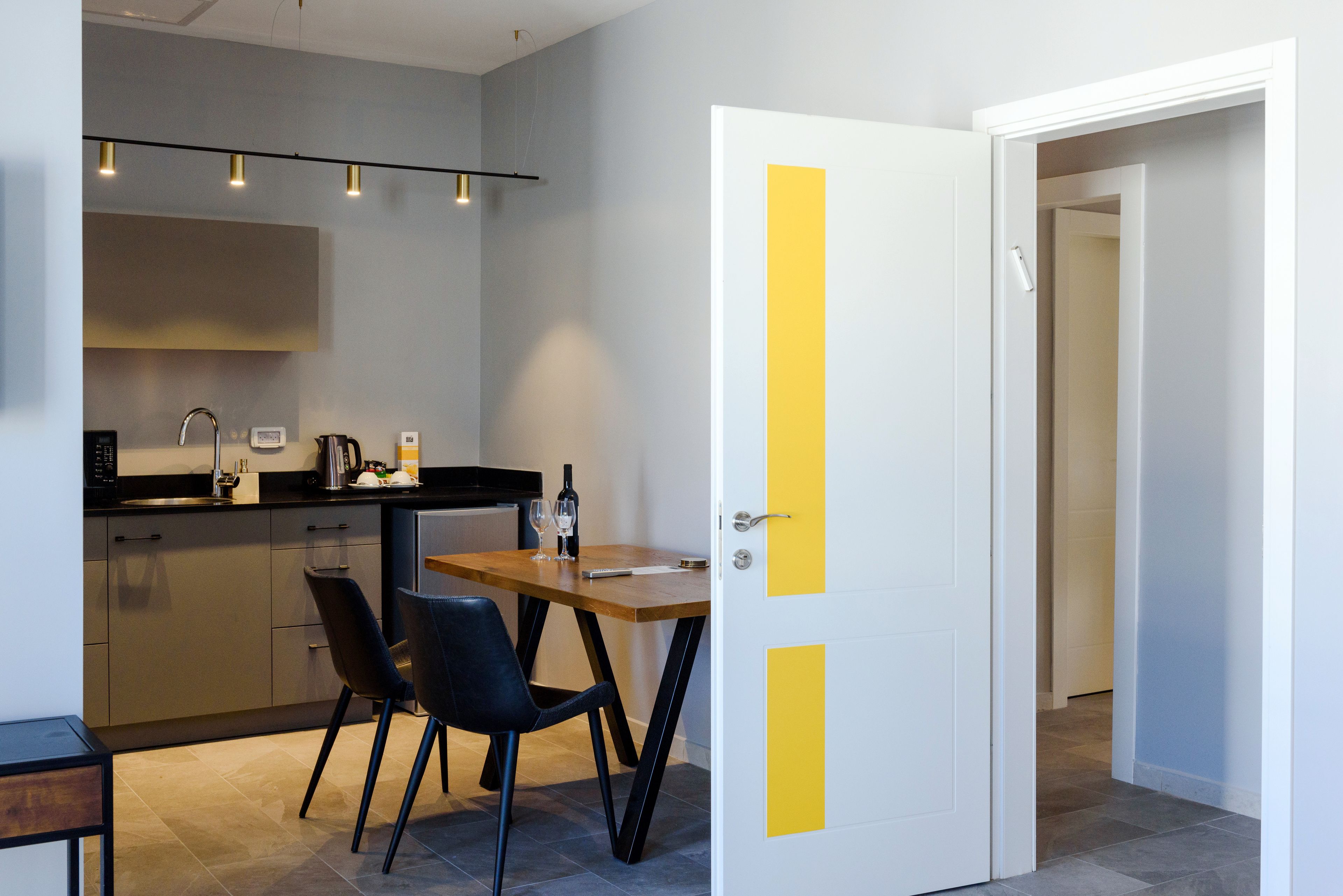 A modern kitchen with a dining area, featuring a wooden table and chairs, a built-in oven, and a black countertop.