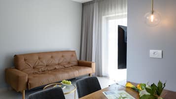 A modern living room with a brown leather sofa, a wooden dining table with chairs, a glass pendant light, and a window with curtains.