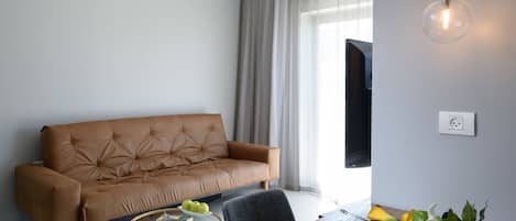 A modern living room with a brown leather sofa, a wooden dining table with chairs, a glass pendant light, and a window with curtains.