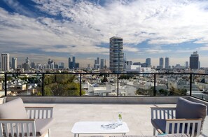 Une terrasse sur le toit offrant une vue sur la ville, avec une table agrémentée de verres et d’une bouteille, ainsi que deux chaises blanches dotées de coussins.