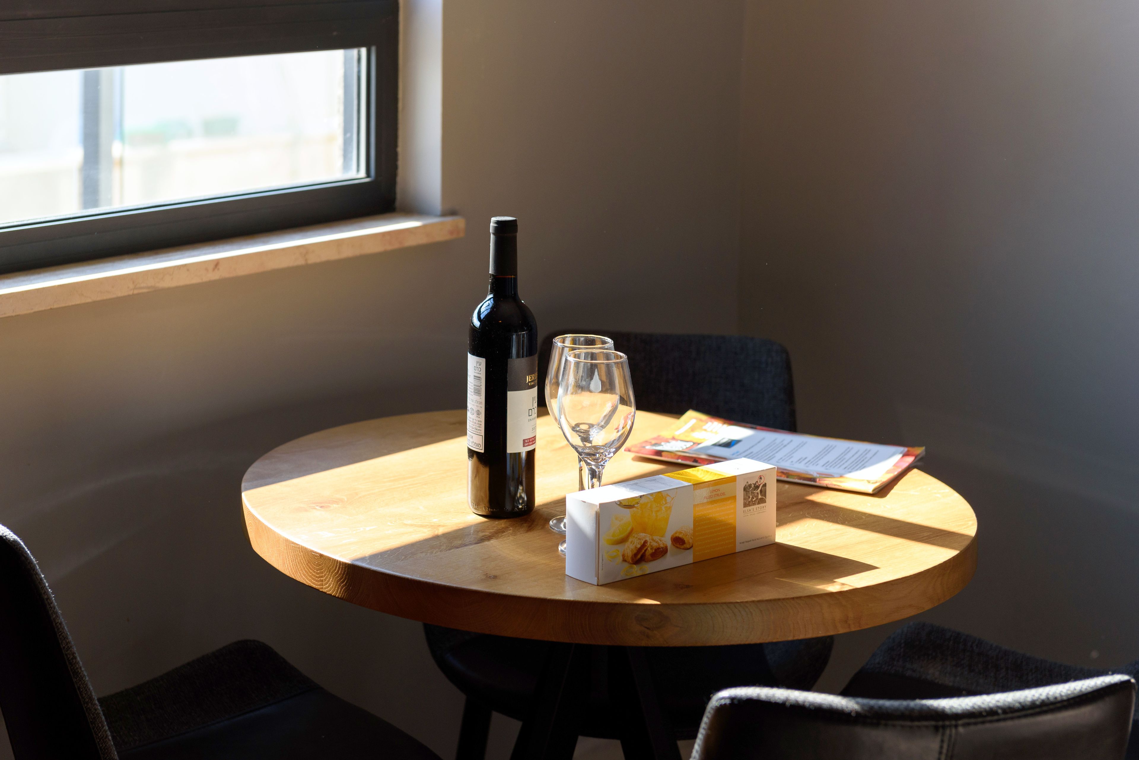 A round wooden table with a bottle of wine, a wine glass, and a box of pastries.