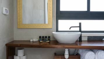 Un baño moderno con tocador de madera, un lavamanos blanco, un espejo grande con marco decorativo y una ventana que proporciona luz natural.