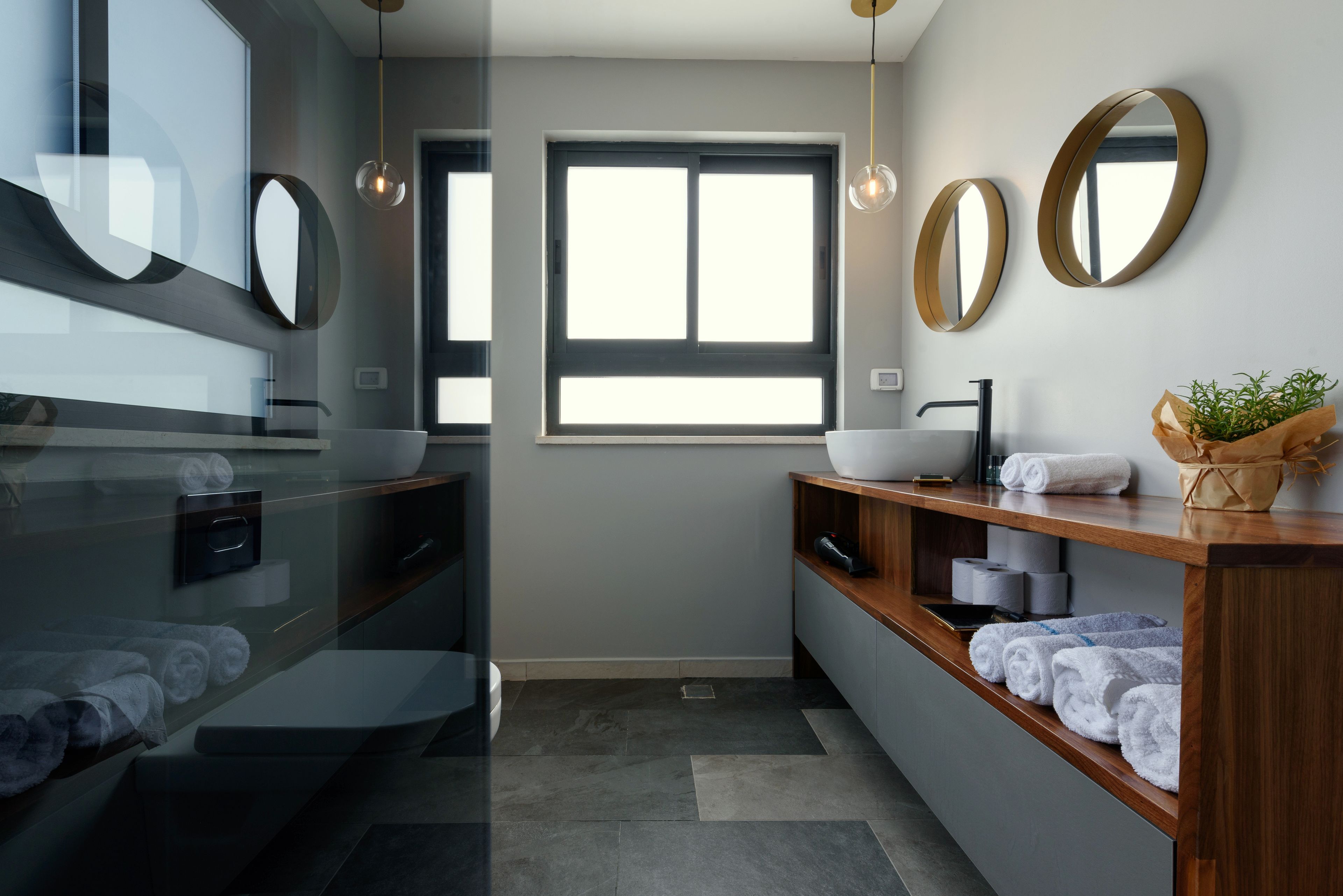 A modern bathroom with a large window, a sink with a vessel basin, and a wooden vanity with towels.