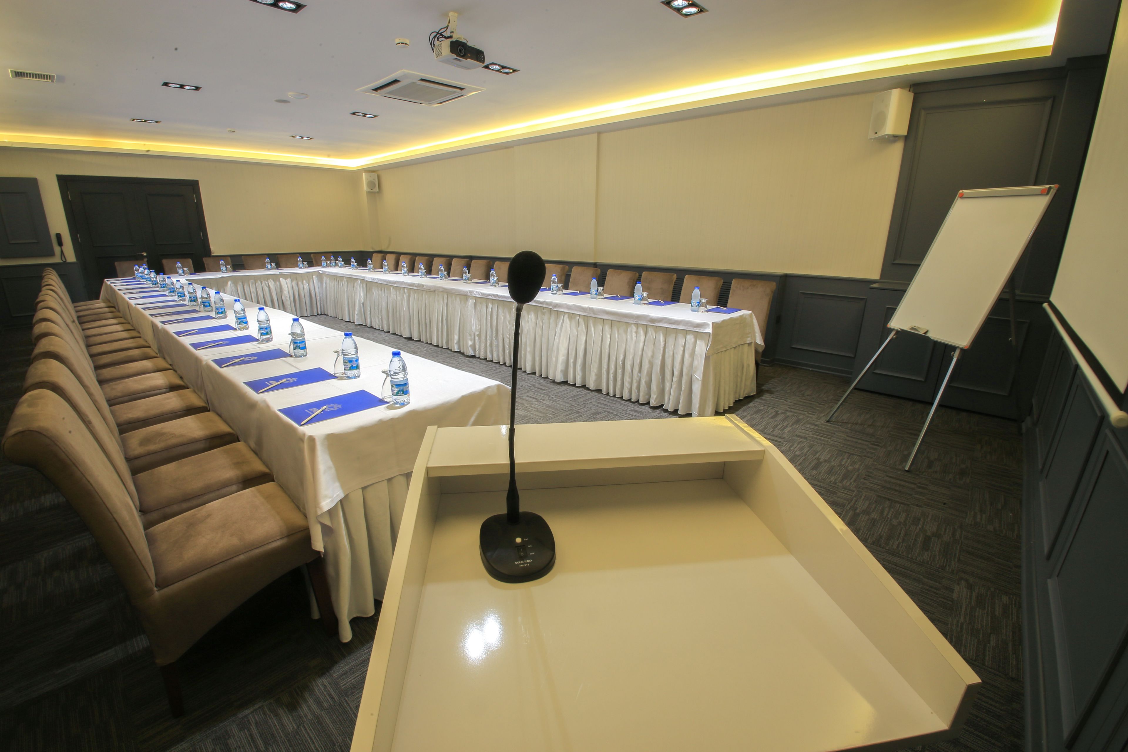 A conference room with a long table, multiple chairs, water bottles, a whiteboard, and a podium.