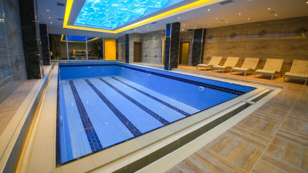 Une piscine intérieure moderne avec un sol carrelé de bleu, un plafond orné de motifs lumineux et un espace détente avec des fauteuils.