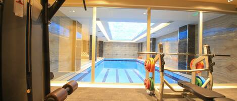 A gym with a view of a swimming pool through glass doors.