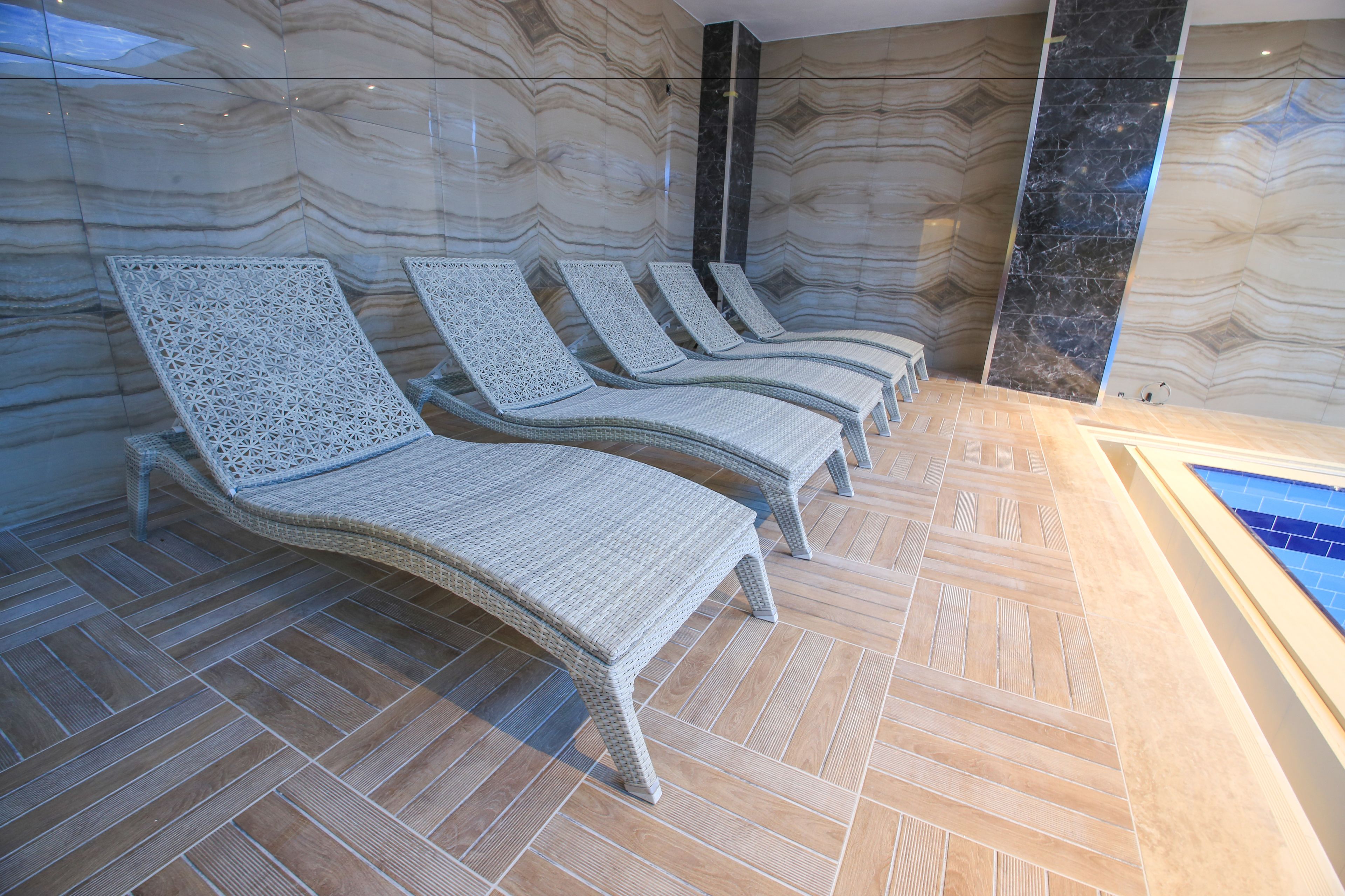 A spa area with four wicker lounge chairs aligned against a wall with a marble pattern.