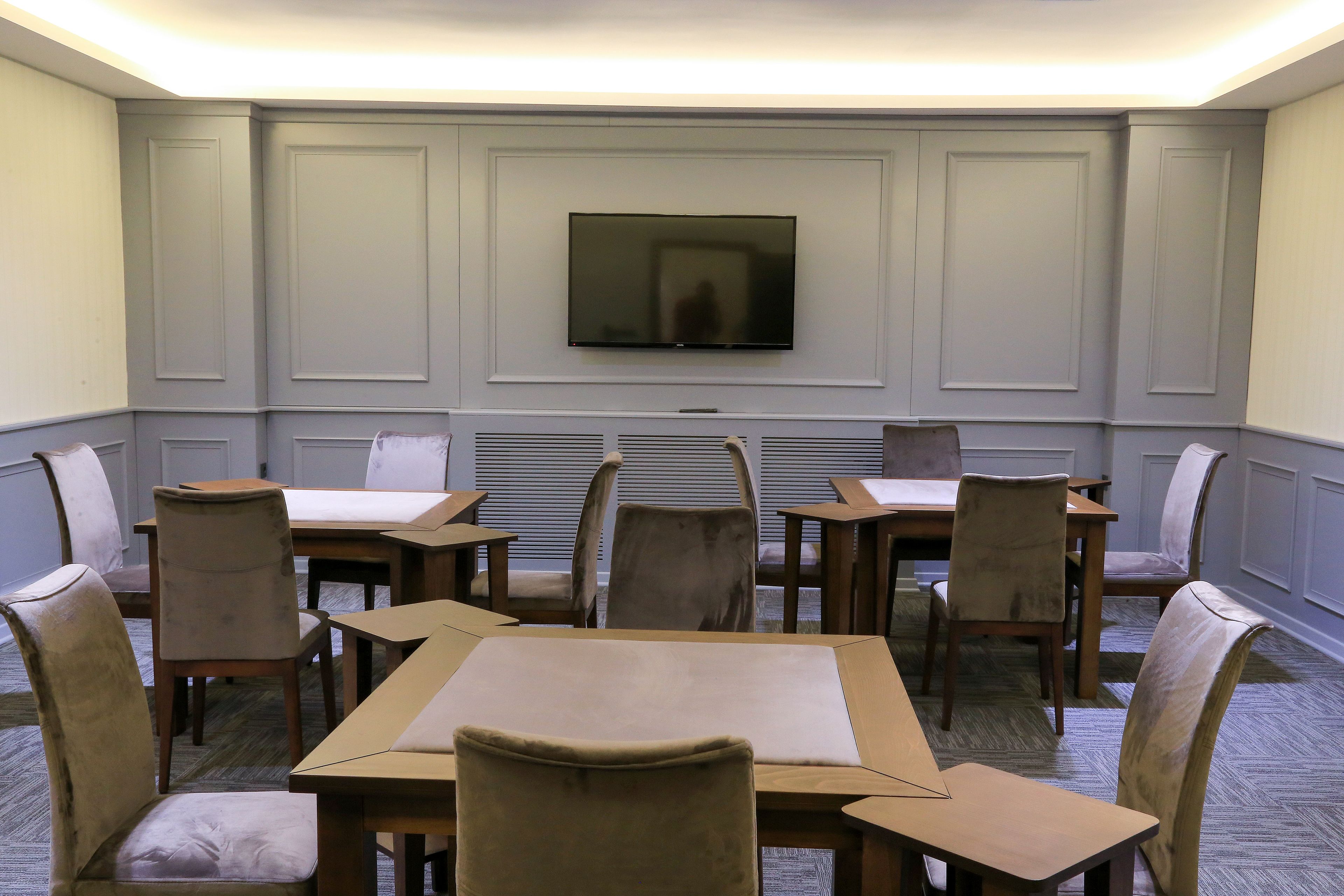 A conference room with a flat-screen TV mounted on the wall, surrounded by wooden tables and chairs.