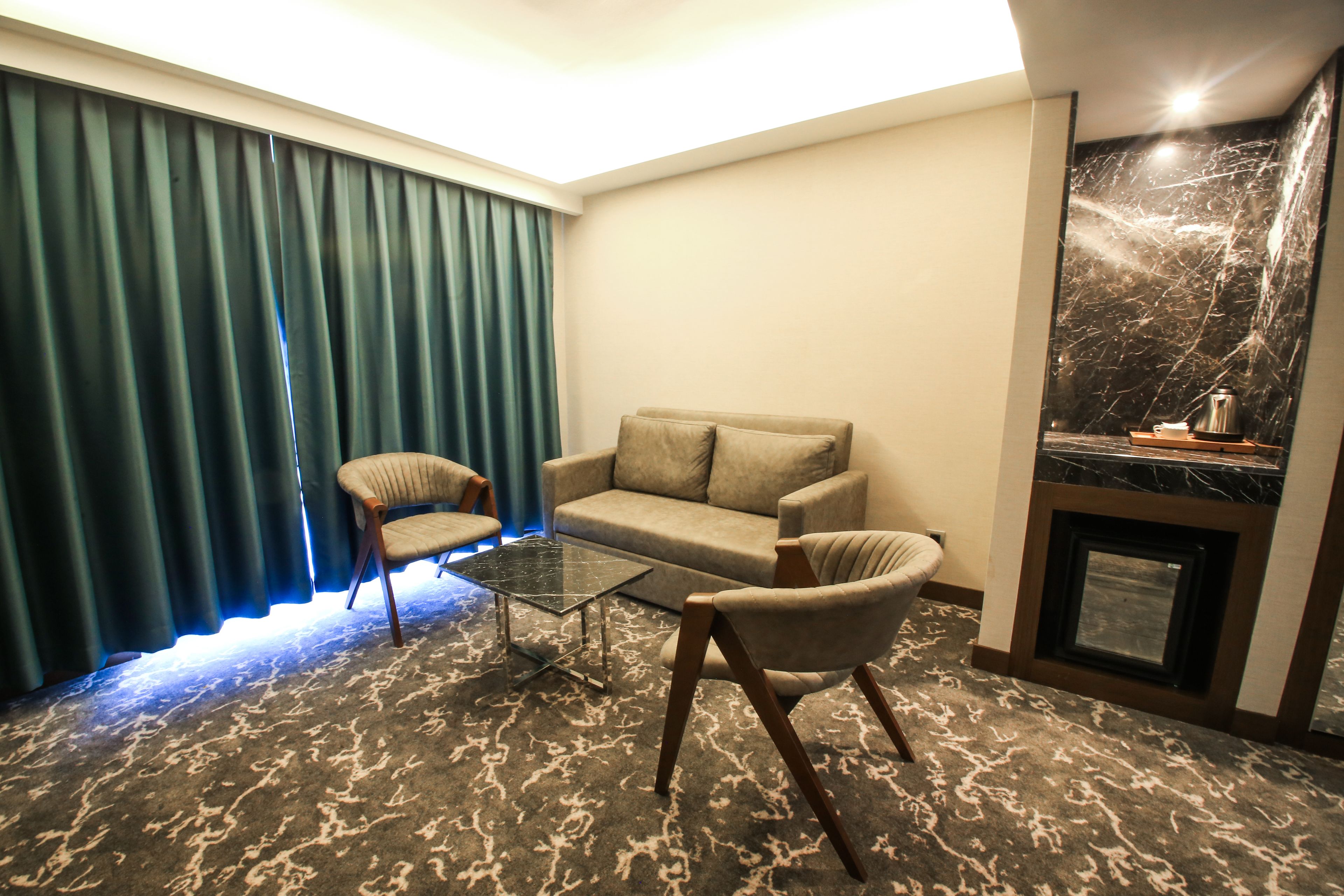 Una habitación con sofá, dos sillones, una mesa de centro de vidrio, chimenea y cortina.