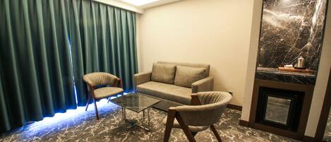 Una habitación con sofá, dos sillones, una mesa de centro de vidrio, chimenea y cortina.