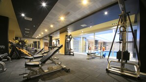 Une salle de sport équipée de divers appareils d’exercice, dotée d’une grande fenêtre et offrant une vue sur une piscine.