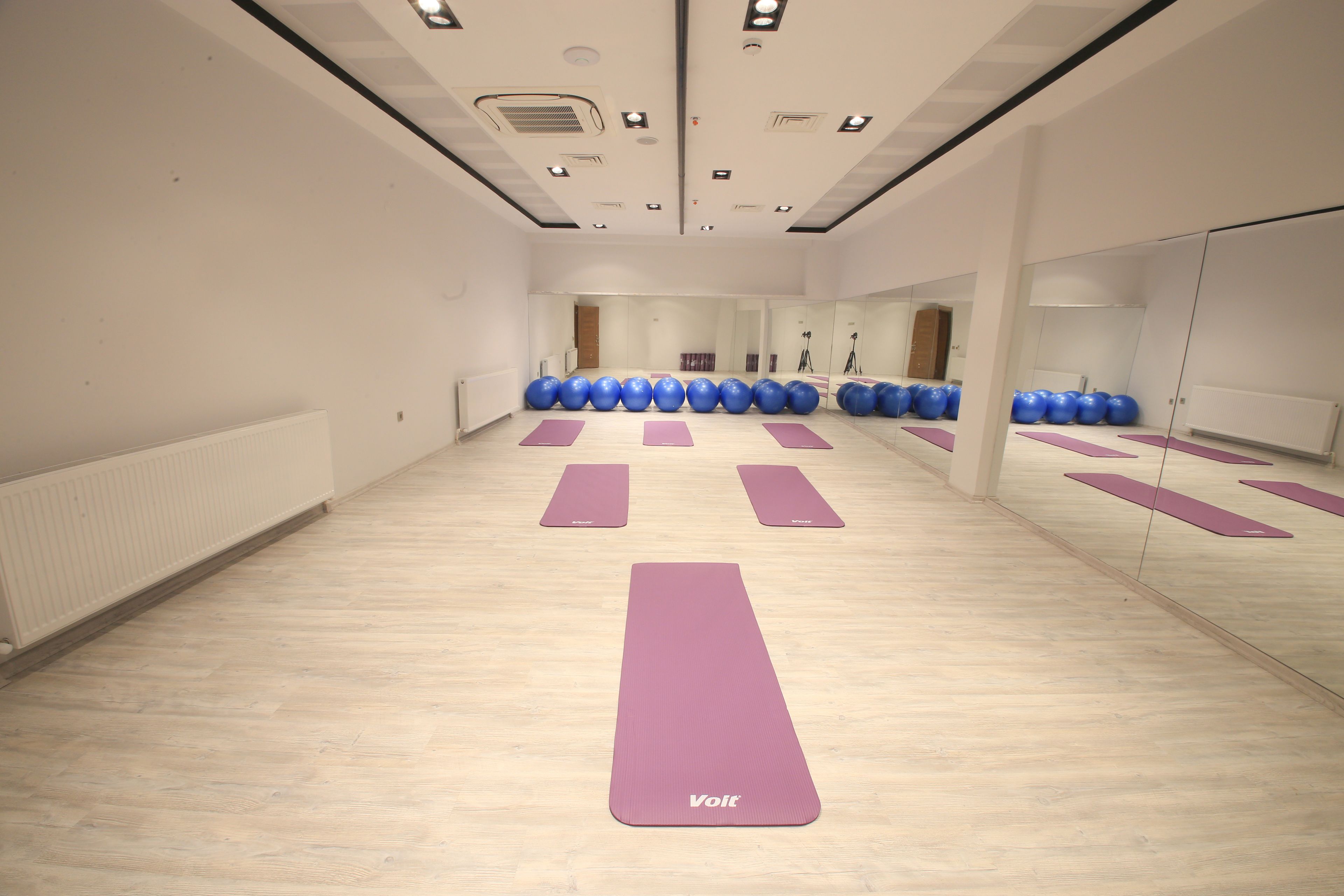 Een ruime kamer met een spiegelwand, houten vloer en yogamatten.
