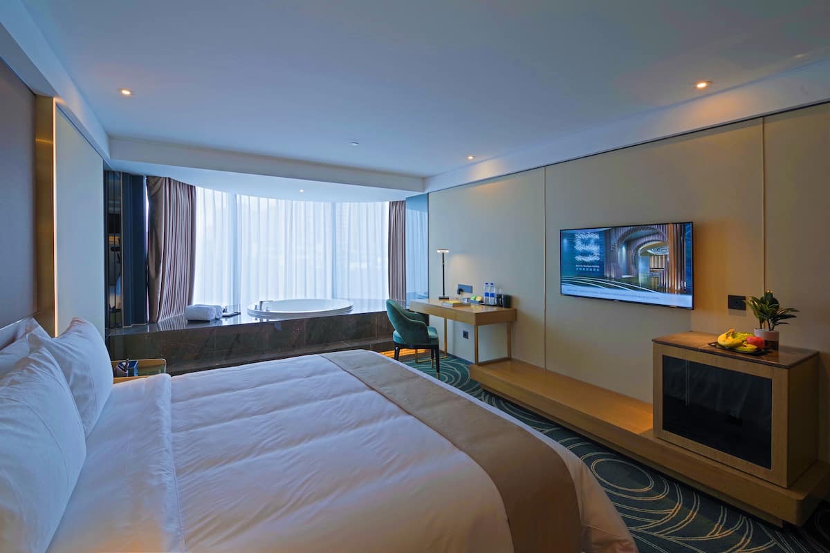 Een hotelkamer met een groot bed, een bureau, een stoel, een televisie en een raam met gordijnen.