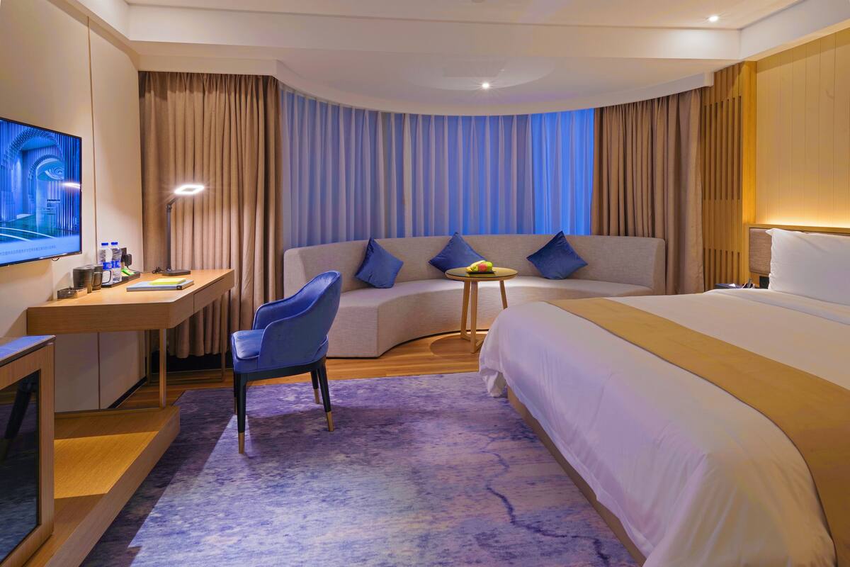 Een moderne hotelkamer met een gebogen bed, een bureau, een stoel en een televisie.