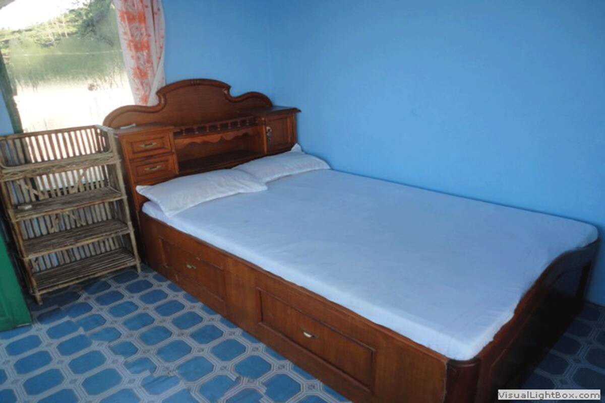 Uma cama de solteiro com cabeceira de madeira e uma estante de metal ao lado.