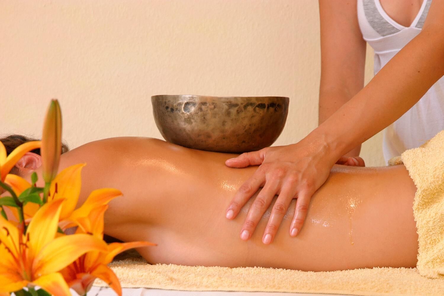 A person receiving a massage with a bowl and flowers on the table.