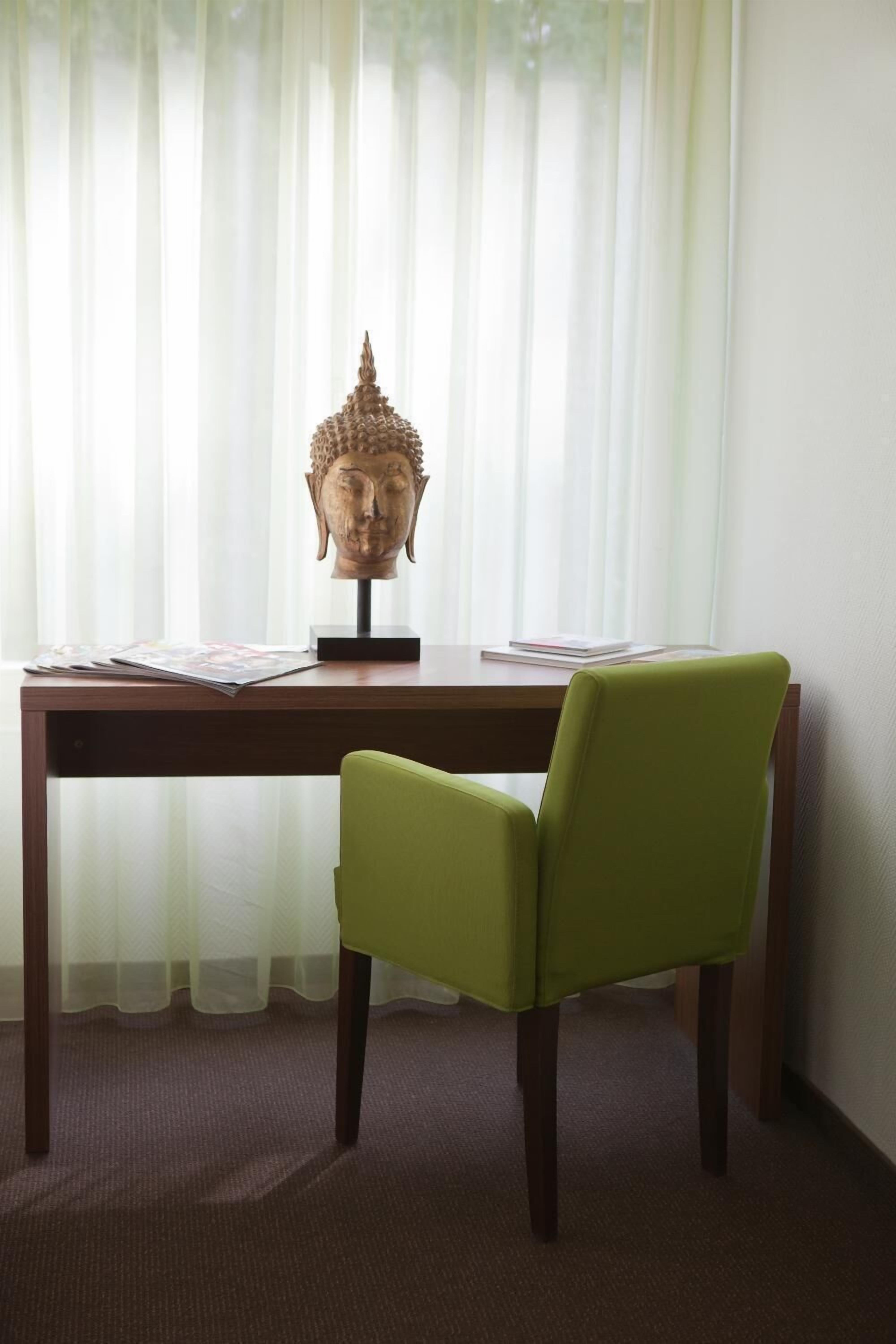 A room with a wooden desk, a green chair, and a Buddha head sculpture on the desk.