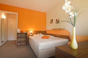 Ein Hotelzimmer mit einem Bett, einem Nachttisch, einer Lampe, einer Vase mit Blumen und einem Regal mit Gegenständen.