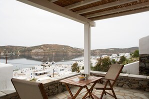 A terrace with a table and chairs overlooking a coastal town with white buildings and a calm sea.
