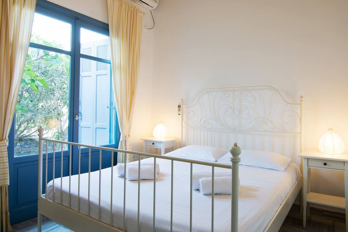 Un lit en métal blanc avec une tête de lit, deux tables de chevet avec des lampes et une fenêtre avec des rideaux.