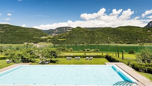 A swimming pool with lounge chairs and a view of a lake and mountains. - Hotel Hasslhof (Caldaro Sulla Strada del Vino)