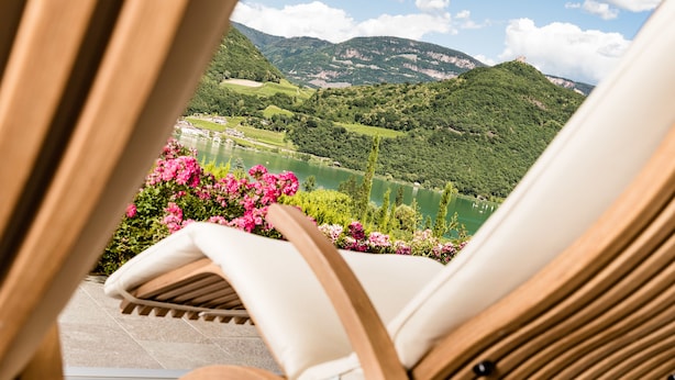 A view from a balcony with a chair and flowers, overlooking a lake and mountains. - Hotel Hasslhof (Caldaro Sulla Strada del Vino)