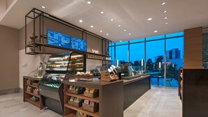Ein modernes Café mit Selbstbedienungstheke, einer digitalen Speisekarte und Blick auf die Stadt durch große Fenster.