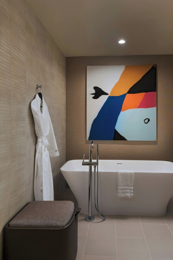 Un baño moderno con una bañera independiente, un perchero con una bata blanca y un cuadro abstracto colorido en la pared.