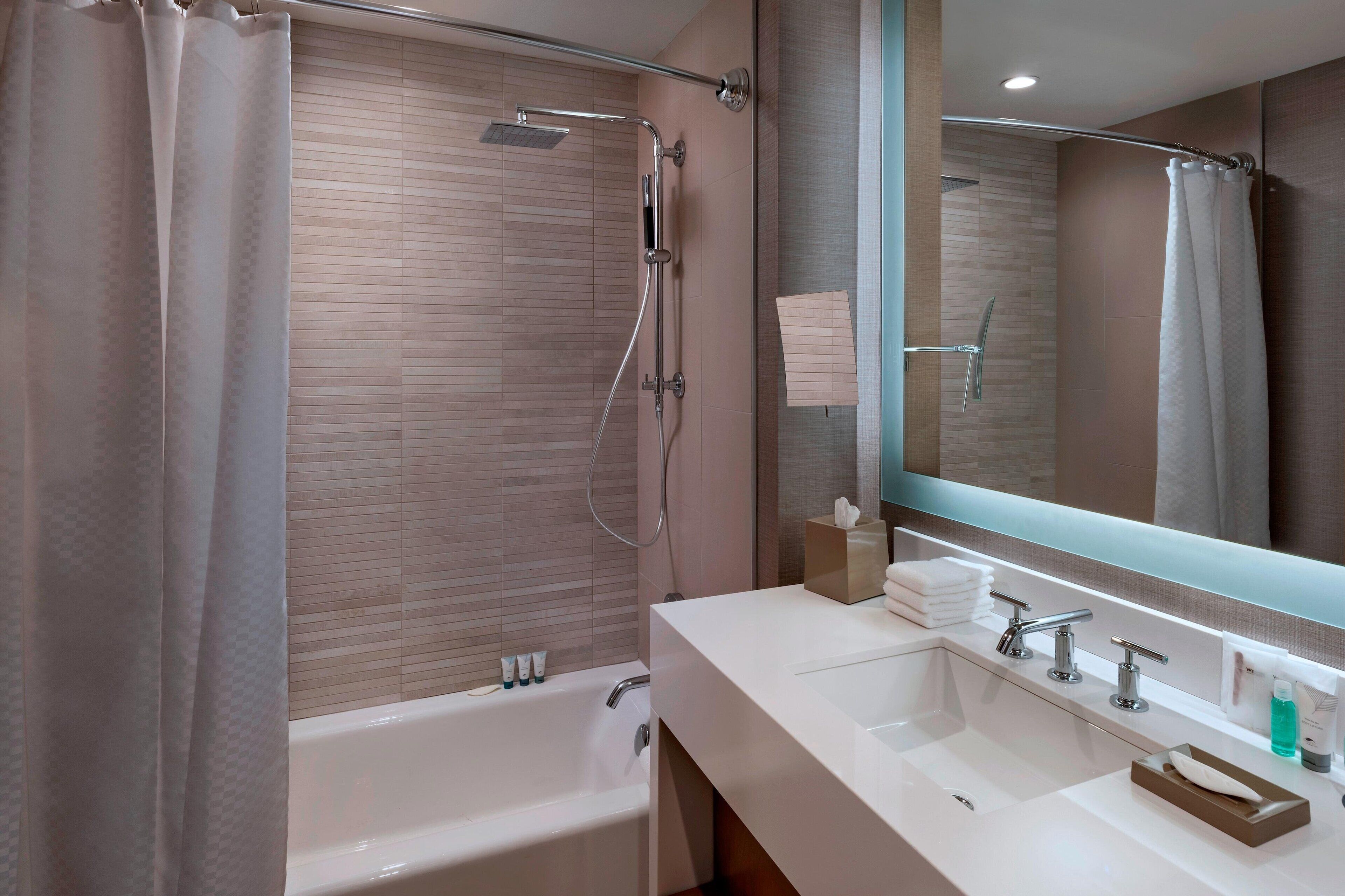 A modern bathroom with a bathtub, a shower with a handheld showerhead, a large mirror, and a vanity with a sink and multiple faucets.