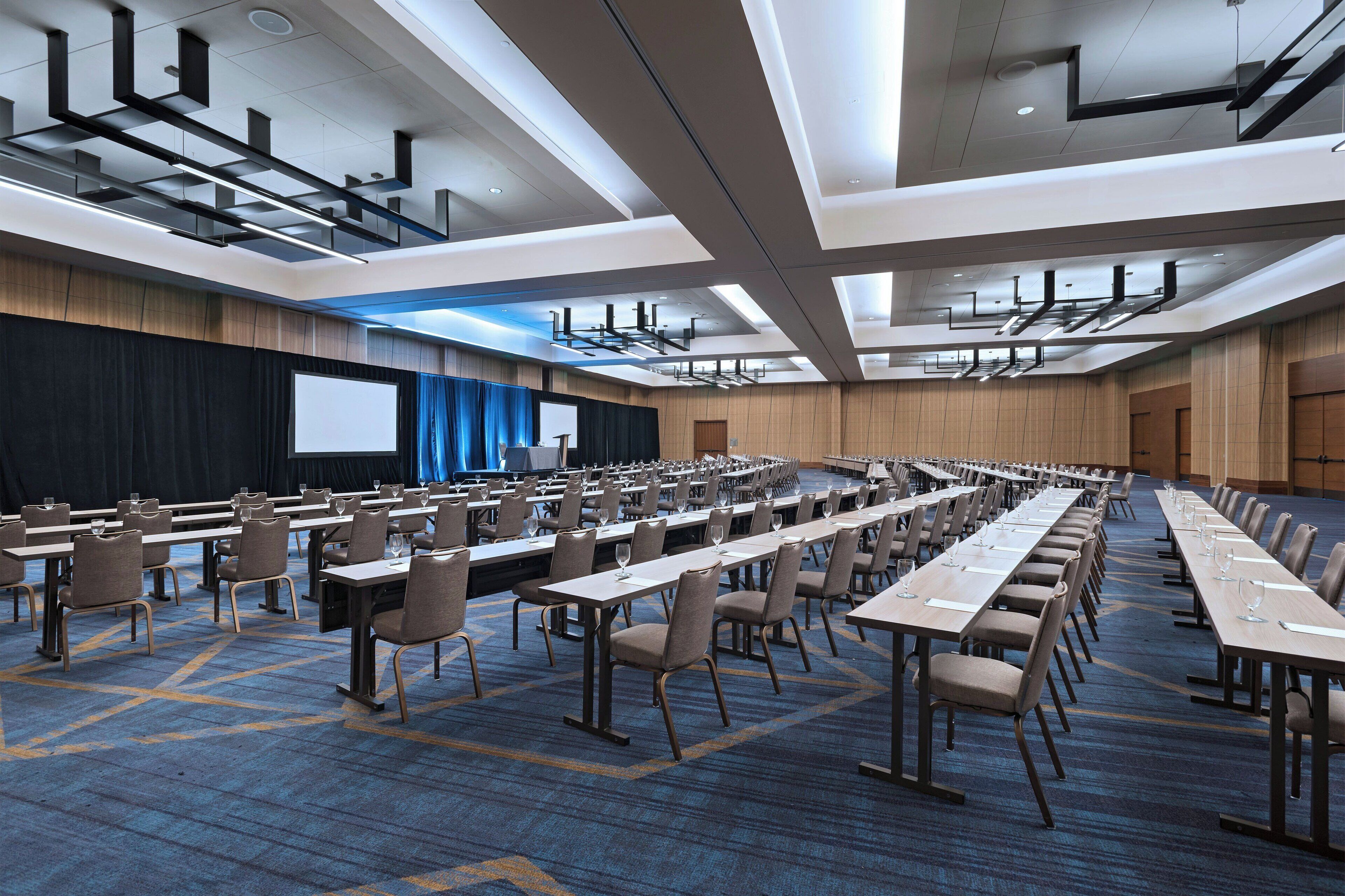Un salón de conferencias con mesas largas, sillas y una pantalla grande.