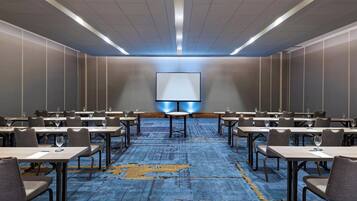 Un salón de conferencias con una pantalla grande, varias mesas y sillas dispuestas para una reunión.