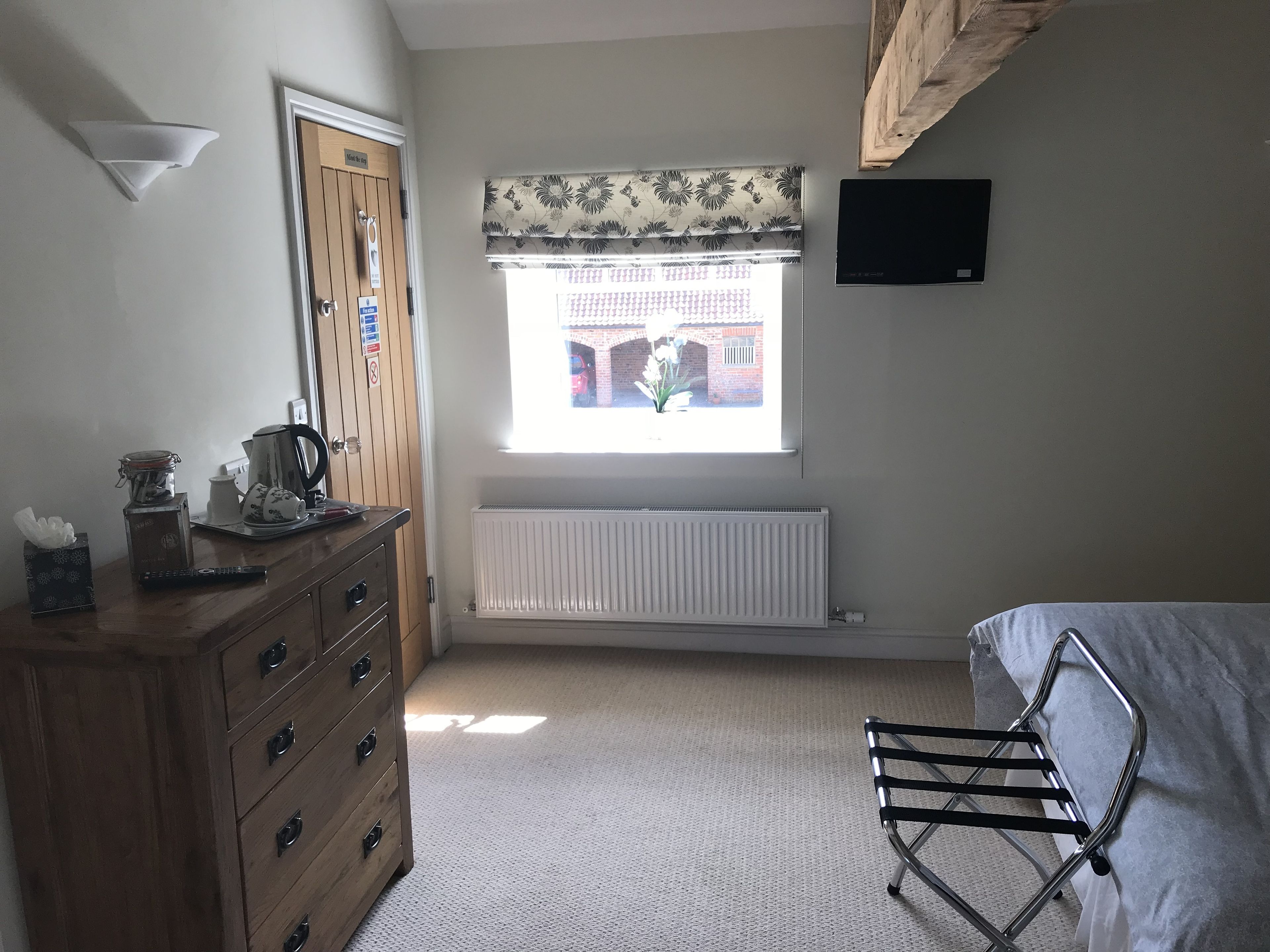 A bedroom with a wooden dresser, a radiator, a window with floral curtains, and a bed with a metal frame.