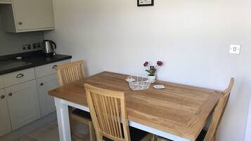 Ein Holztisch mit Stühlen, einem Wasserkocher, einer Topfpflanze und einem gerahmten Bild an der Wand.