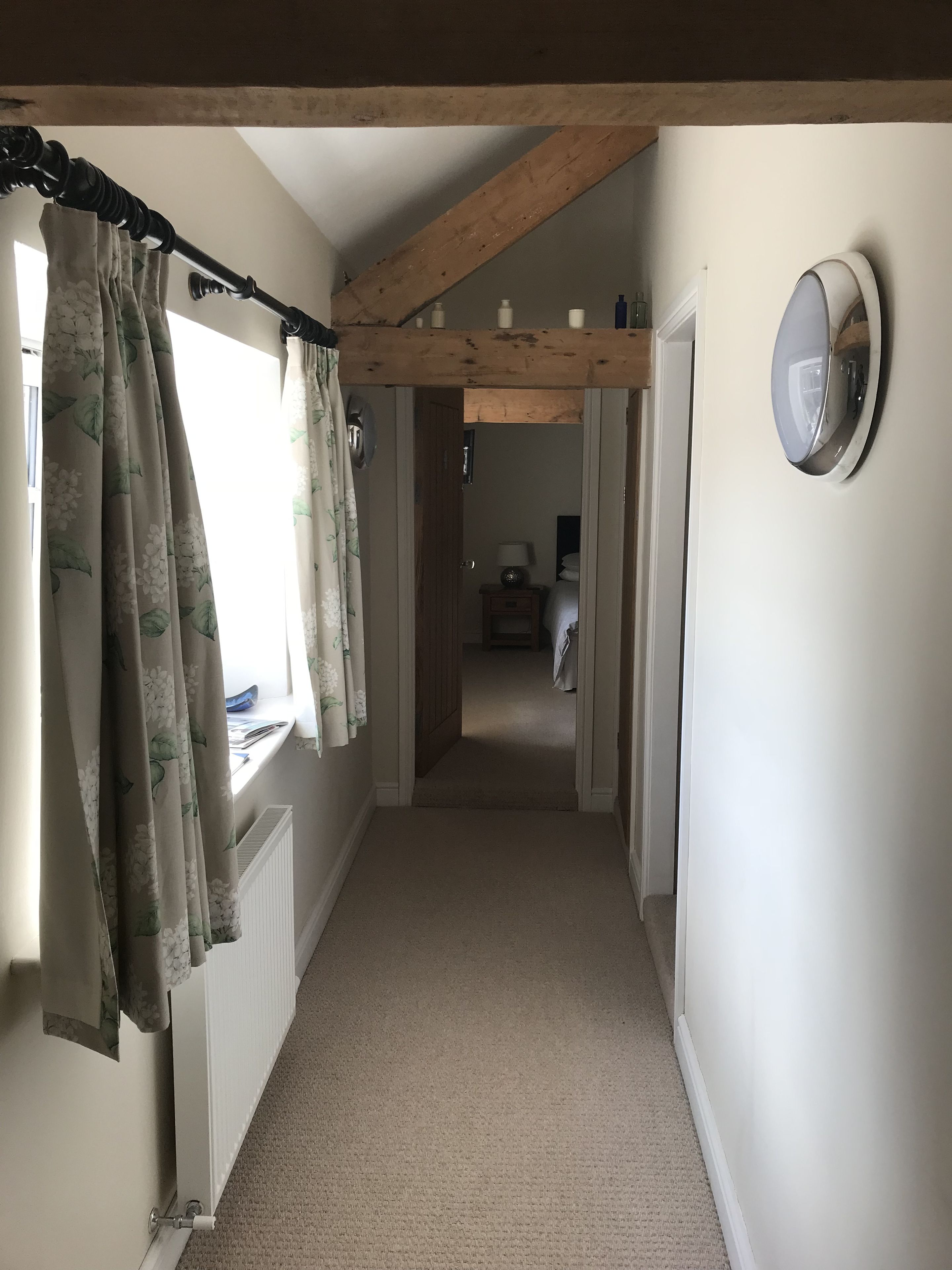 A narrow hallway with a wooden ceiling, a radiator, and a window with floral curtains.
