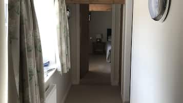 A narrow hallway with a wooden ceiling, a radiator, and a window with floral curtains.