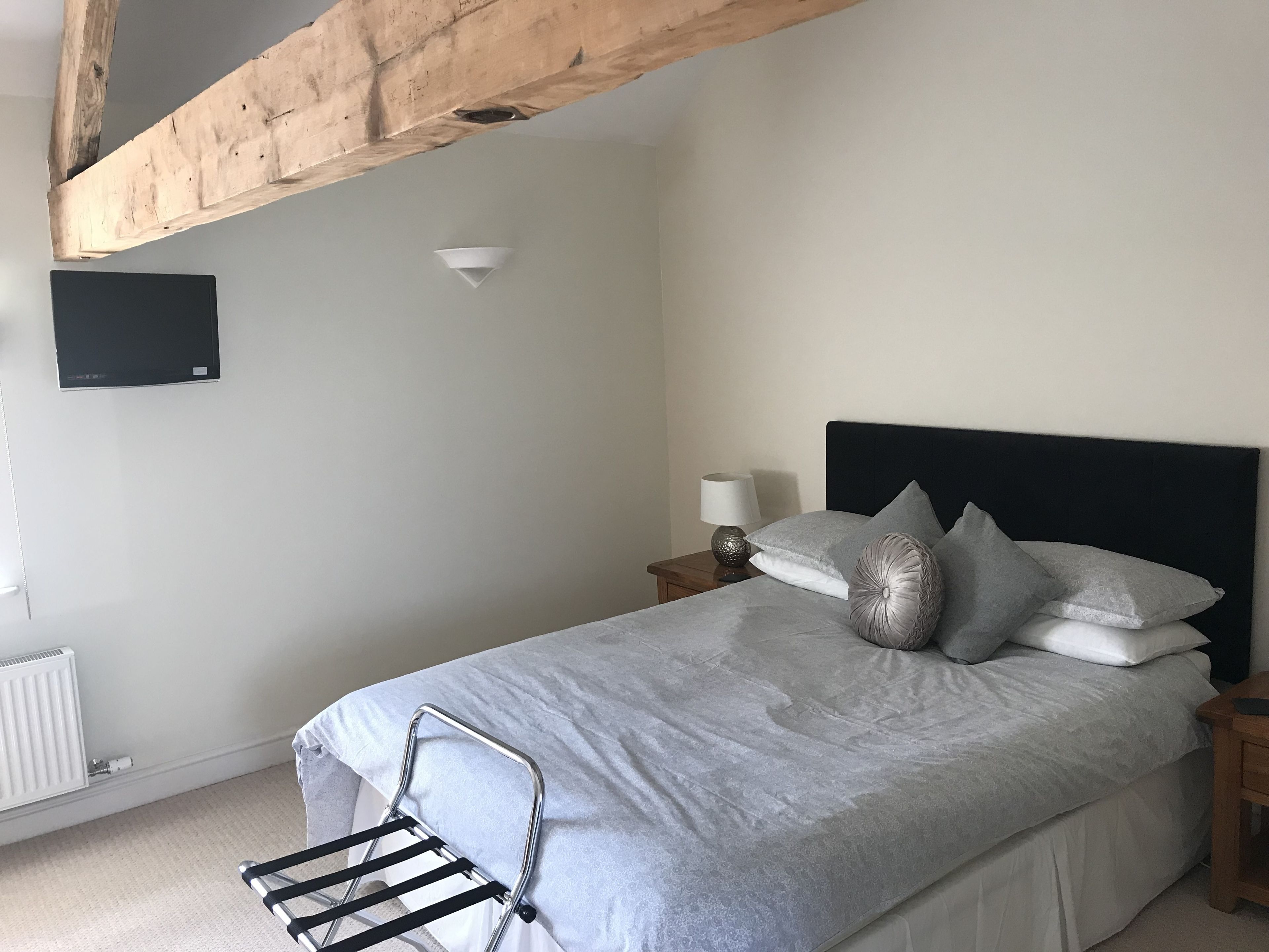 A bedroom with a bed, a nightstand, a lamp, a TV, and a radiator.