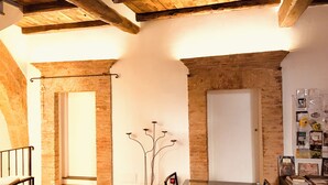 An interior with exposed brick walls, a wooden ceiling, a glass table, and a red chair.