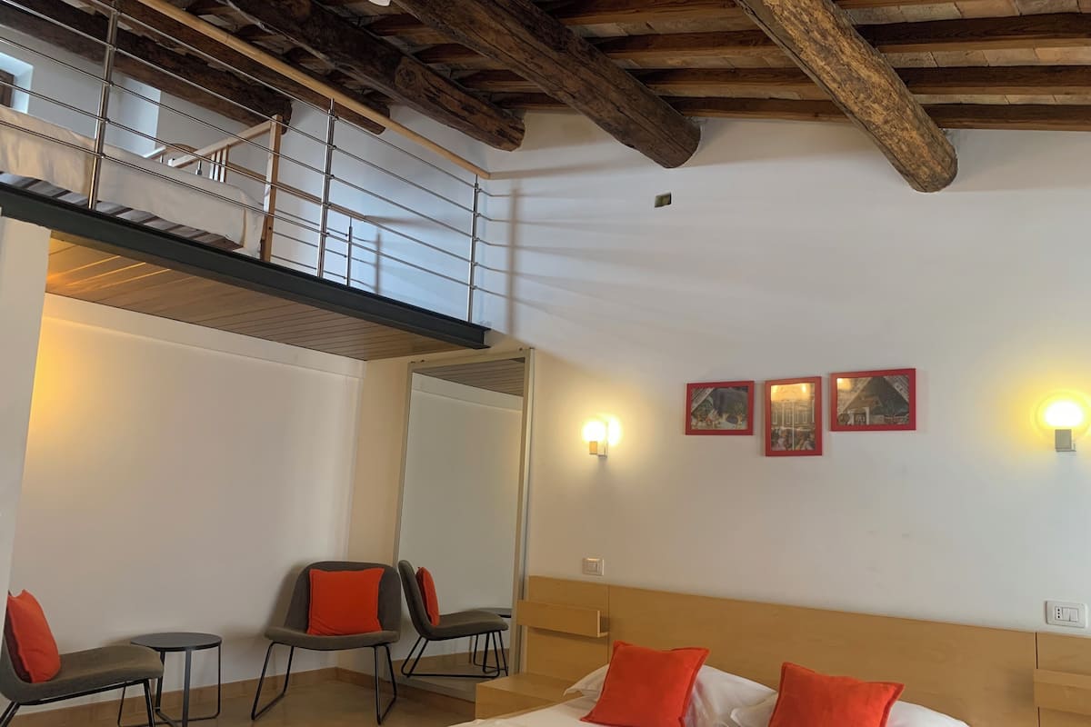 A hotel room with a bed, two chairs, a small table, a mirror, and a wooden ceiling.